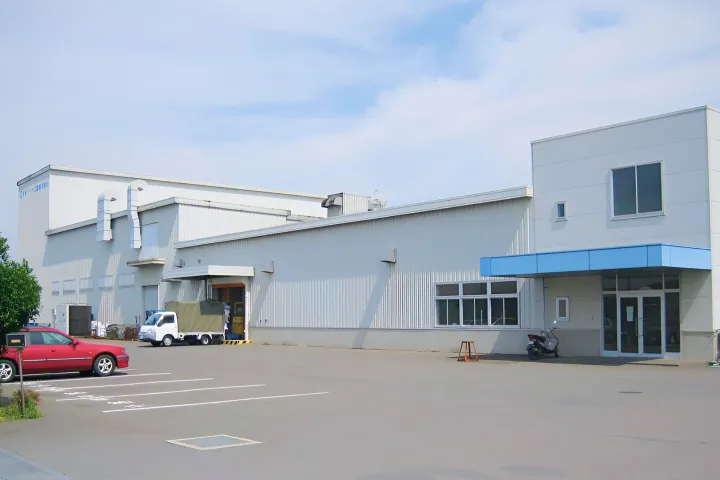 白い外壁と青い屋根の庇を持つ工場建物の外観