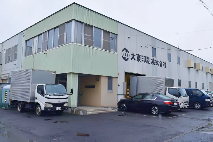 緑と白の外壁を持つ印刷会社の工場建物の外観